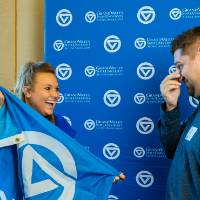 An alumna laughing while holding on to the GV flag, while another alumnus laughs